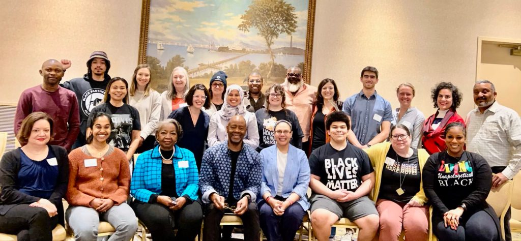 A group photo of about 25 smiling people, diverse in race and age, in a conference room.