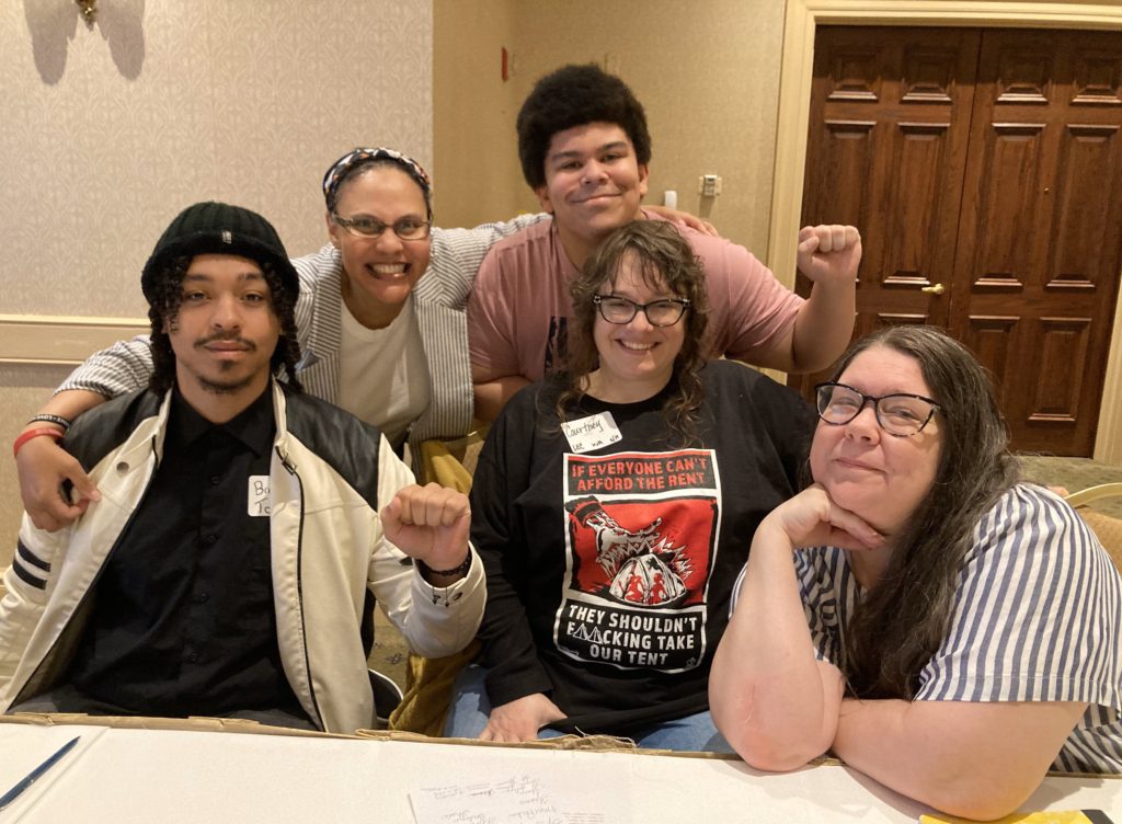 Five smiling people gathered together for the camera at the S.A.I.H. grantee gathering. Two are holding up a fist in the Black Power sign.